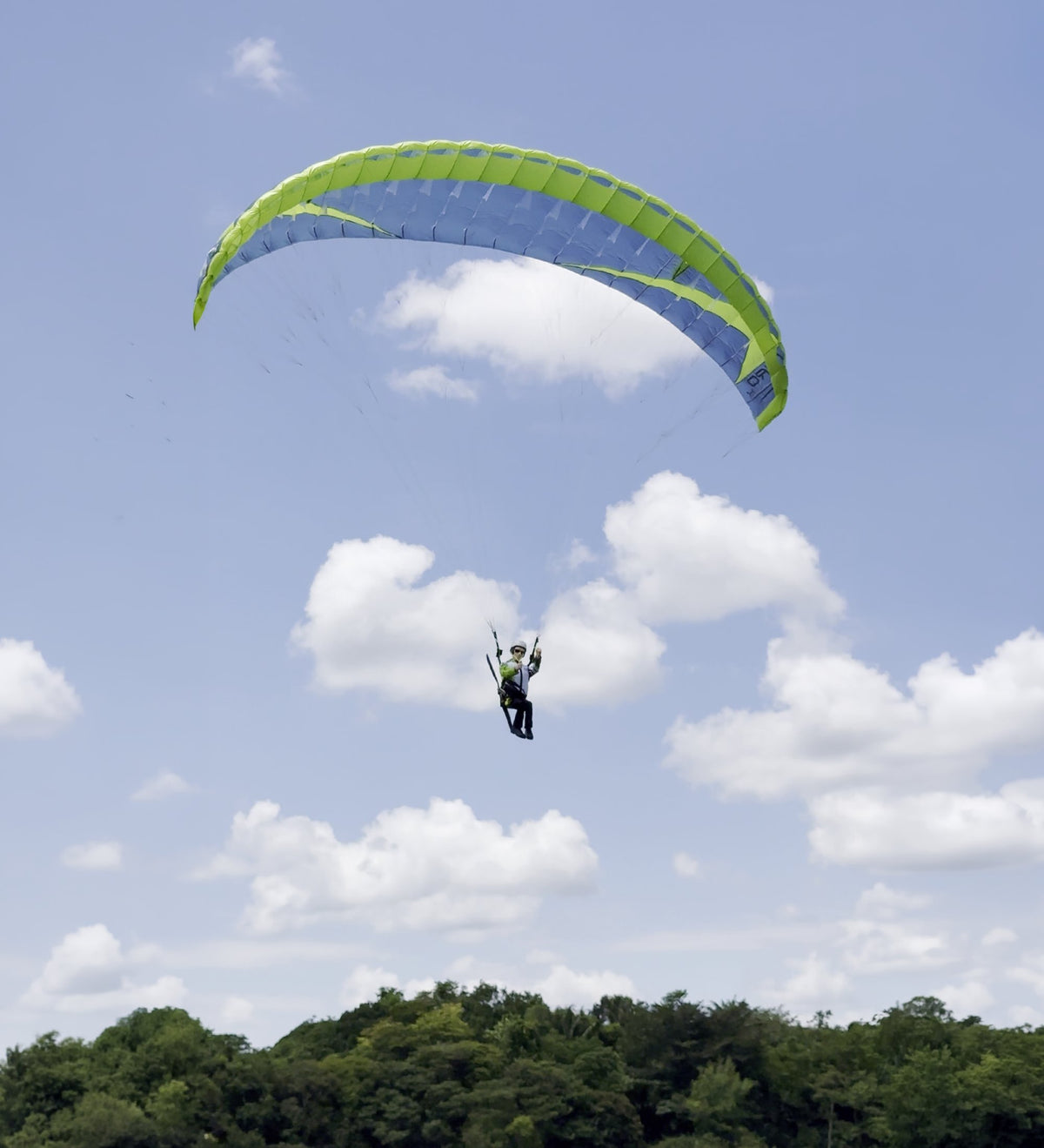 RC-Gleitschirm NYRO X in Slate Blue und Grün im Flug von unten, im Hintergrund Wolken und Bäume
