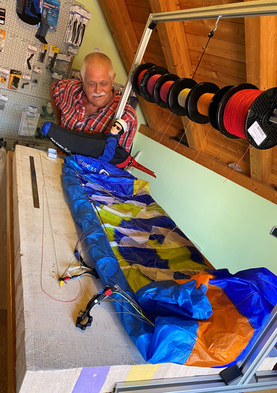 RC-Gleitschirm | RC Paragliding | Leinenreparatur, Mann am Arbeitsplatz uns schaut zu wie sein RC Gleitschirm fachkundig repariert wird.